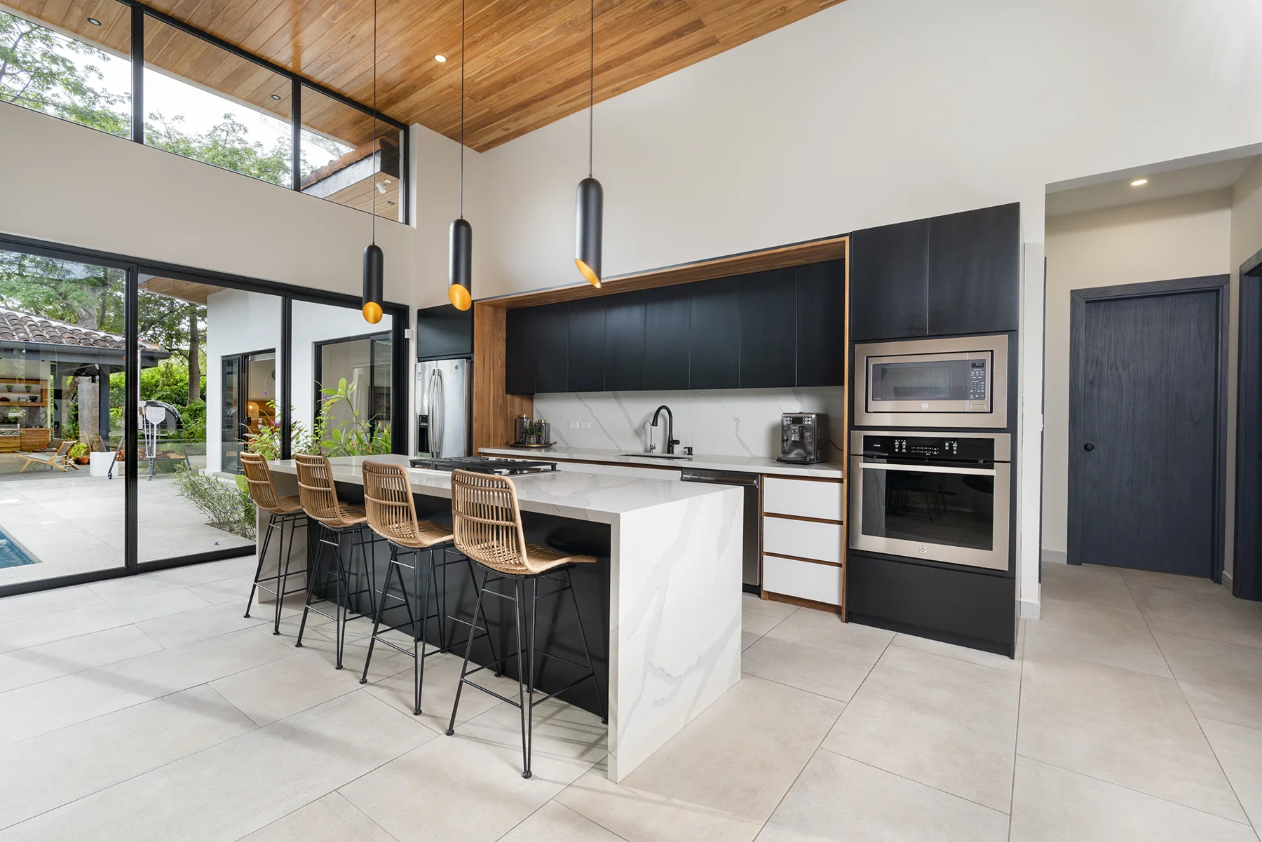 RG69 kitchen with a white island, woven stools and dark cabinetry beneath a timber ceiling
